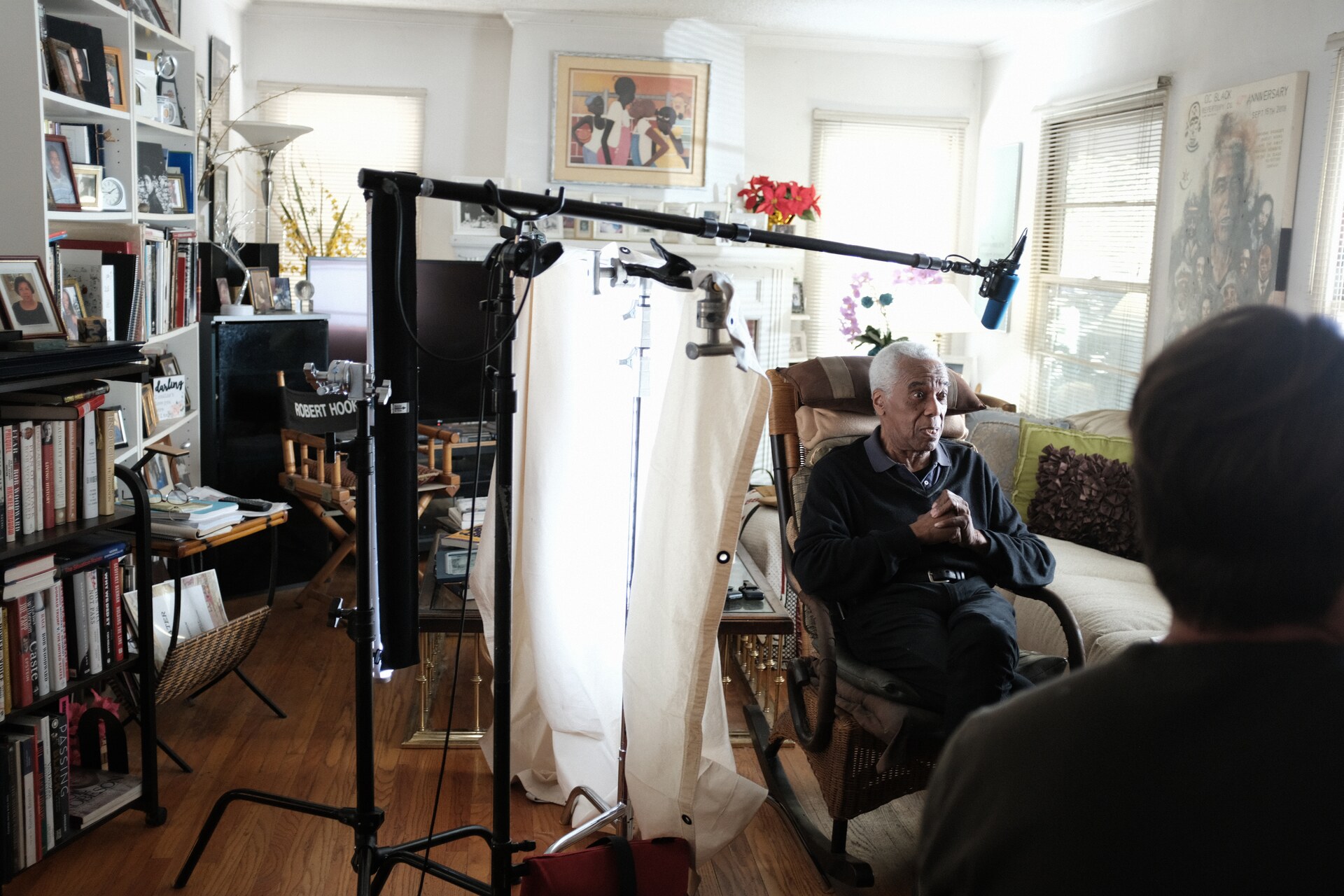 Robert Hooks seated for an interview while a camera crew films inside his home.