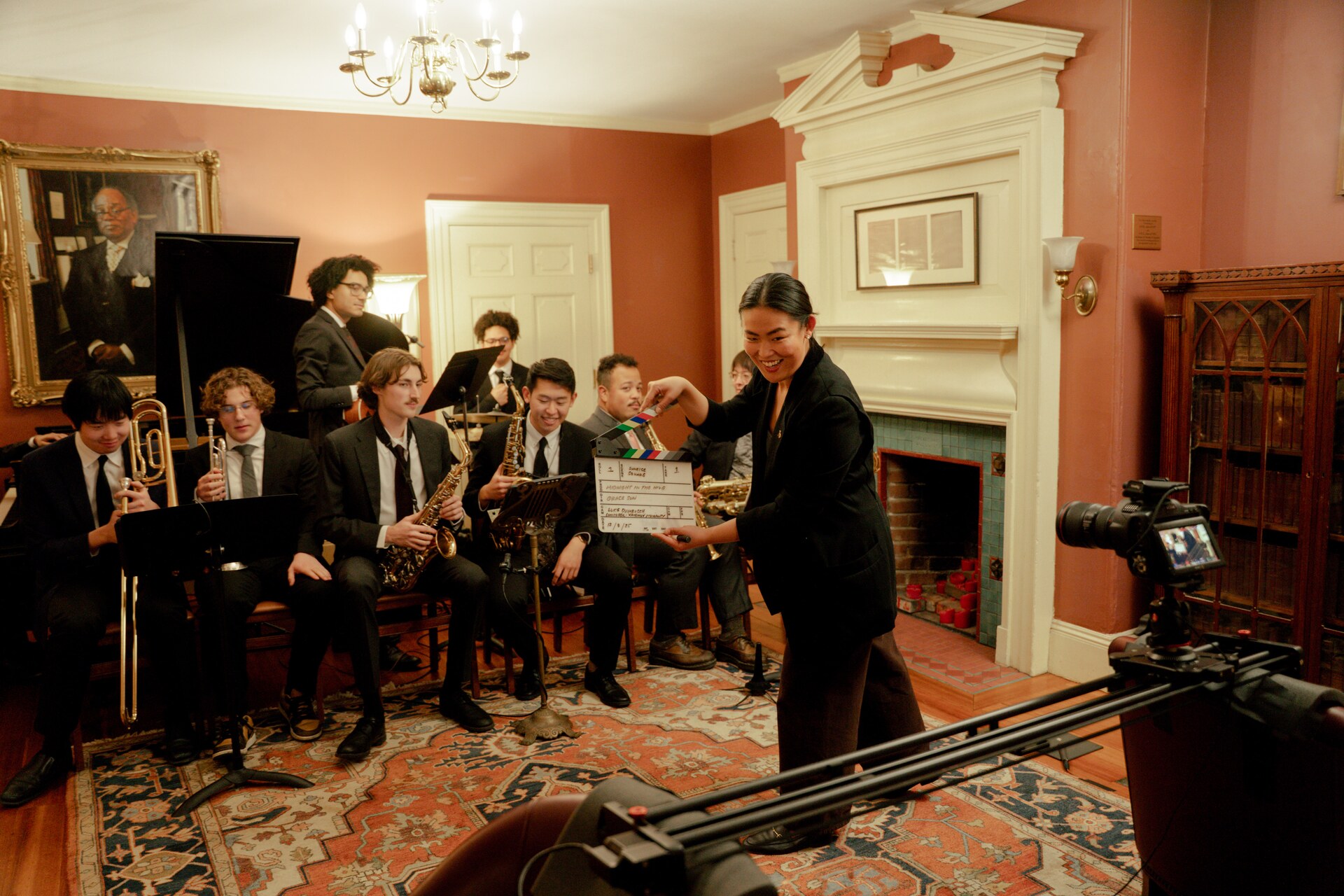 Grace Sun with a film slate in front of a jazz ensemble inside the Signet Society.