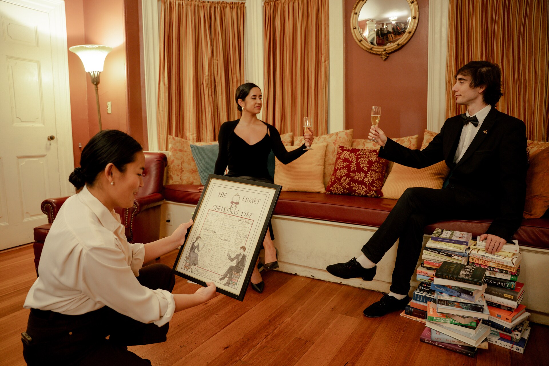 Three performers presenting a framed drawing beside stacks of books in the Signet Society.