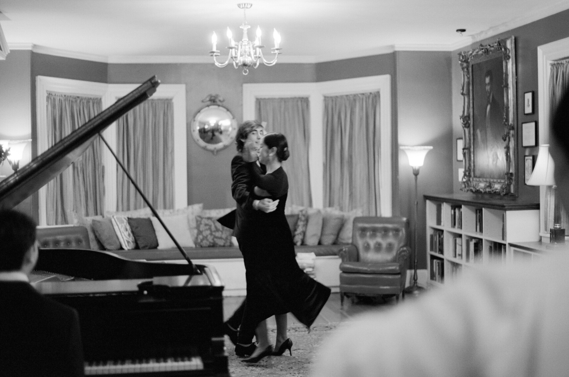 Black-and-white behind-the-scenes image of a dancer performing beside a grand piano.