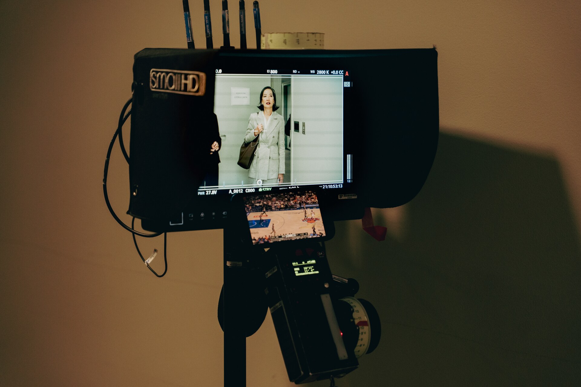 On-set monitor displaying a performer in front of bookshelves.
