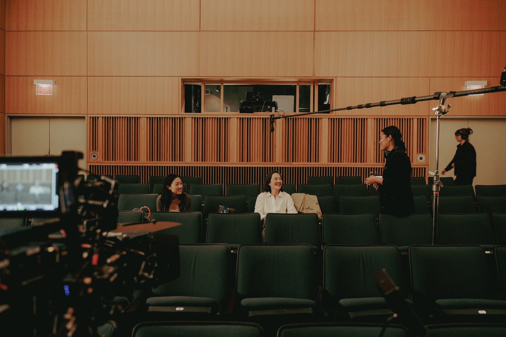 Performers and crew rehearsing among rows of auditorium seats.