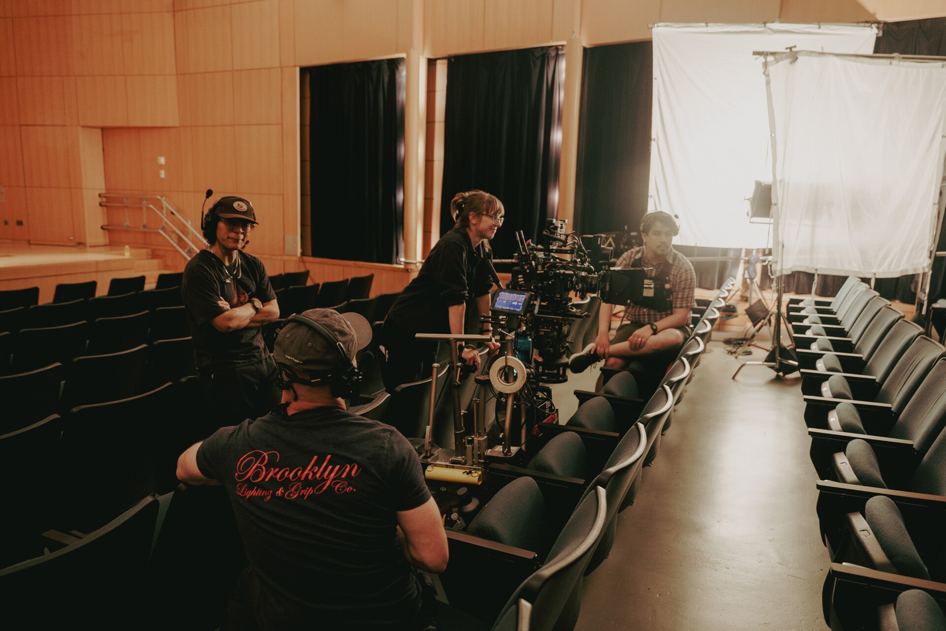 Crew working around a cinema camera and lighting equipment in an auditorium.