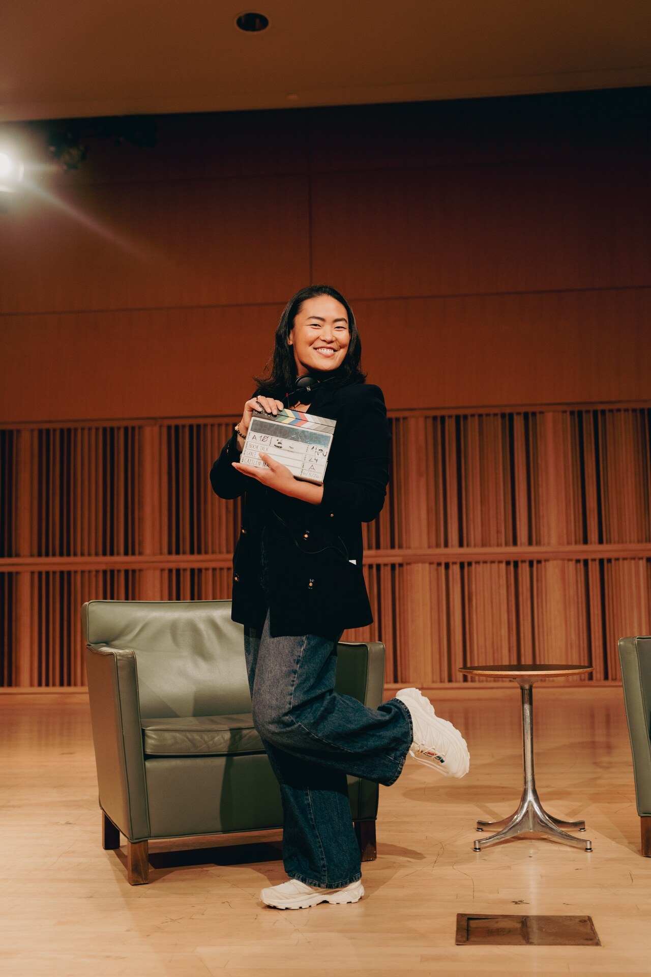 Grace Sun smiling and holding the Book Talk slate in an auditorium.