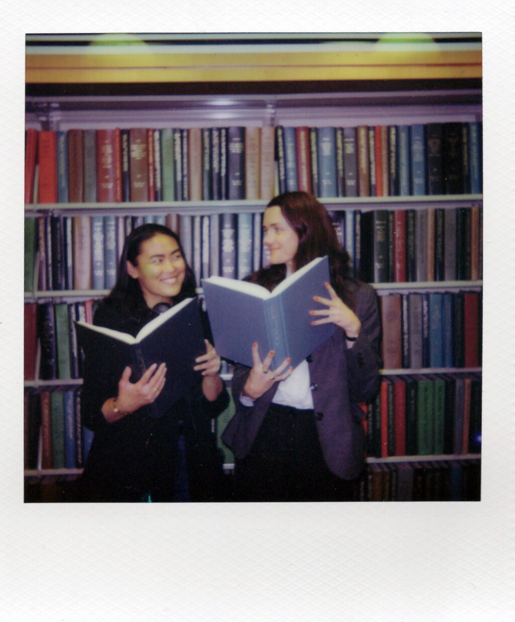 Two women reading together in front of shelves in a Book Talk Polaroid.