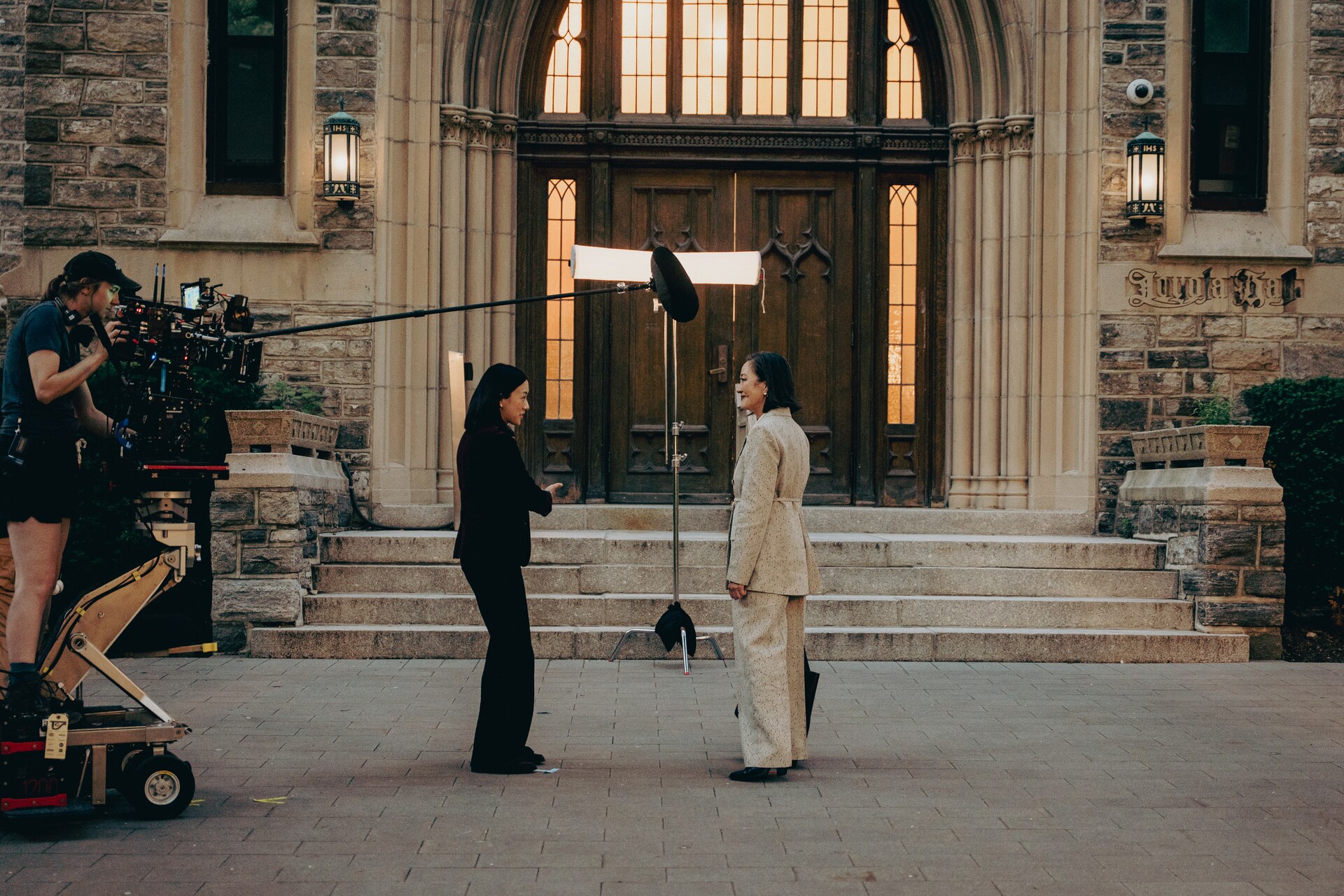 Camera crew filming two women outside a stone library building.
