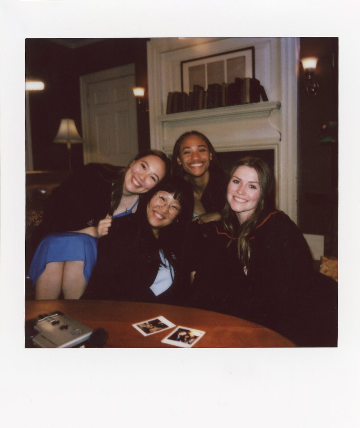 Four friends leaning together around a table in a Commencement Eve Polaroid.