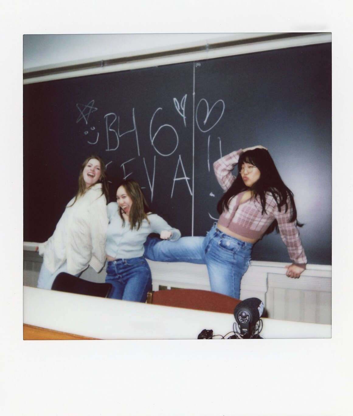 Three friends posing in front of a chalkboard in a Commencement Eve Polaroid.