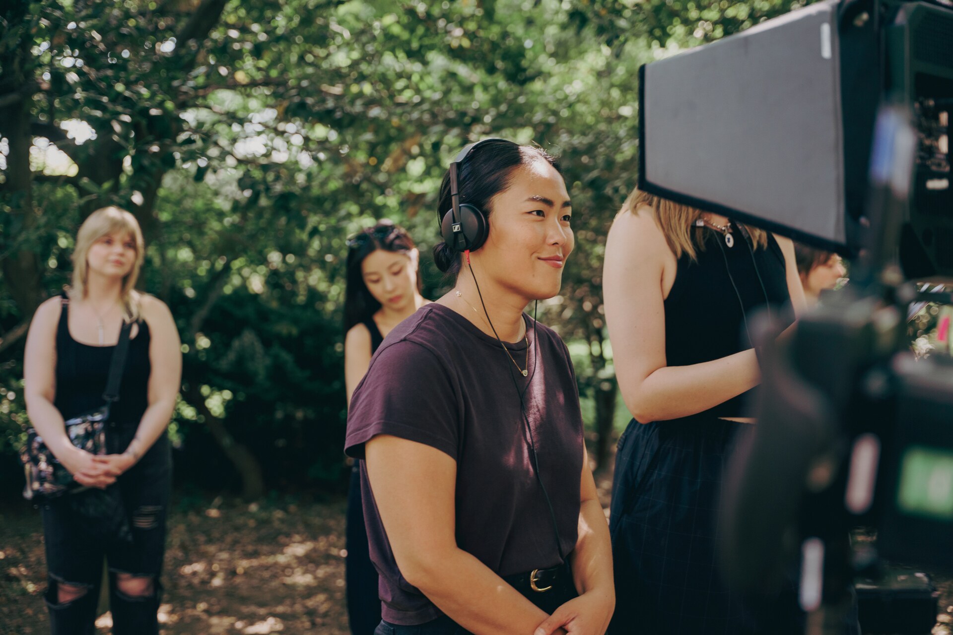 Performer wearing headphones beside a cinema camera during an outdoor film shoot.