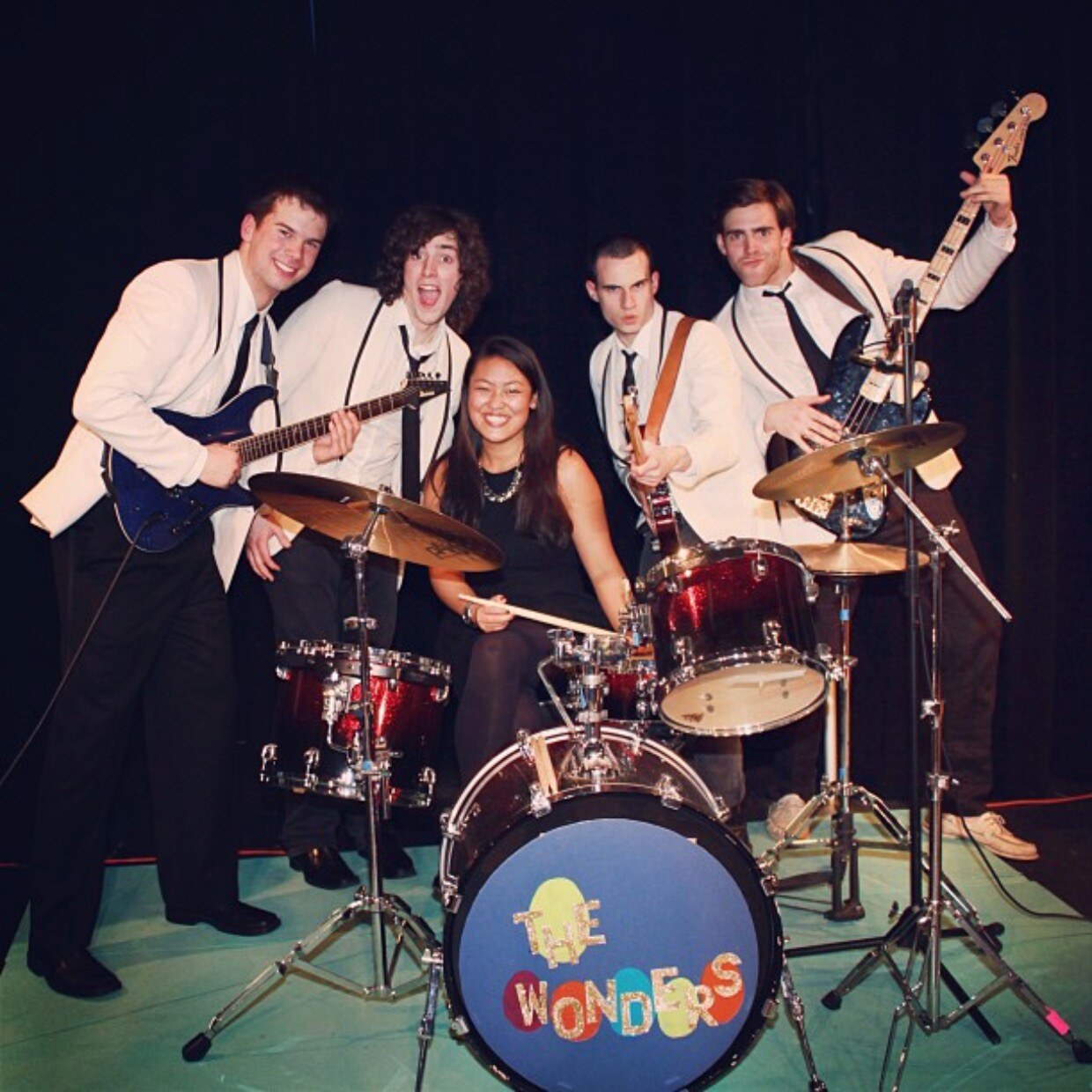 That Thing You Do band and performers posing around a drum kit on stage.