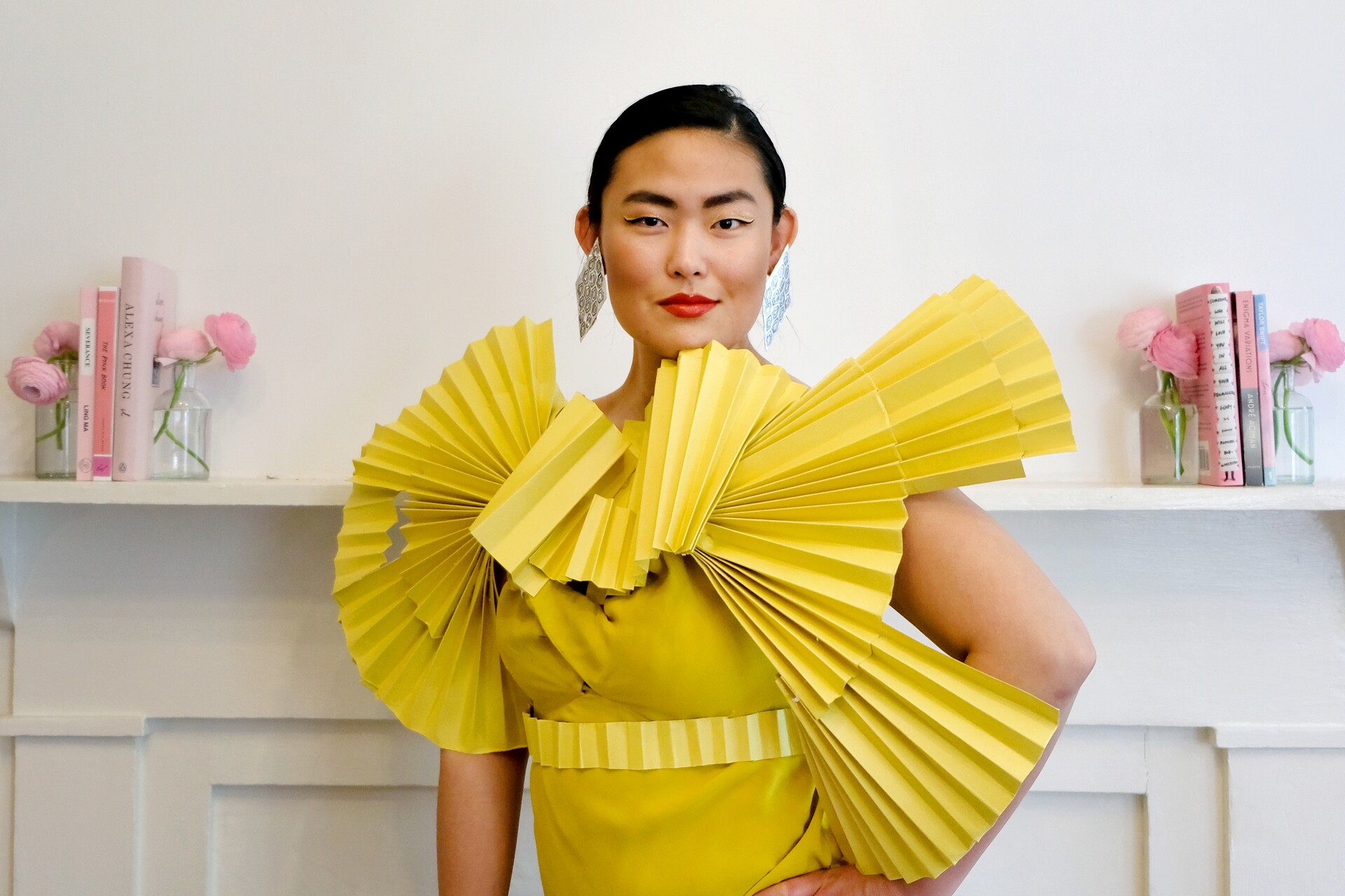 Grace posing indoors in a sculptural yellow costume made from folded paper fans.